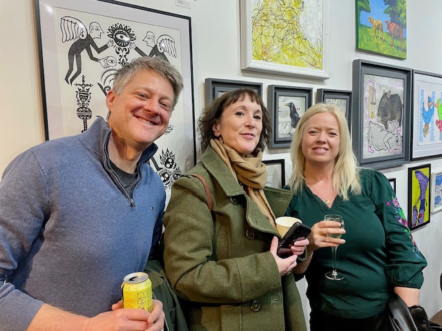 Three CamCreatives members smiling at the camera, standing in front of artwork at the 2026 Art Show.